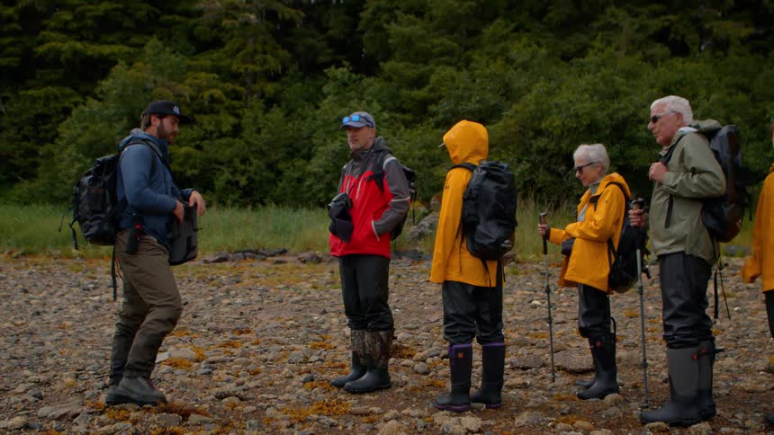 A group of hikers listens attentively to their guide on a rocky shoreline before continuing their trek
