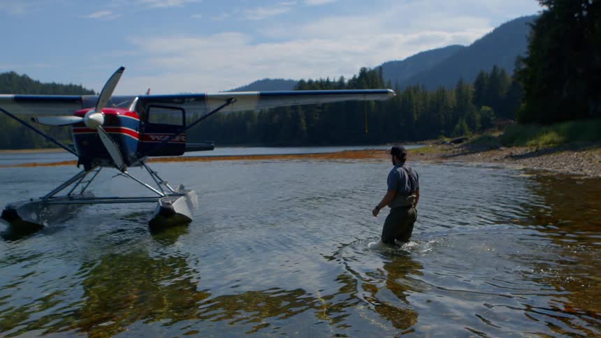 A man in waders watches a seaplane turn in the shallow waters of a remote mountain inlet