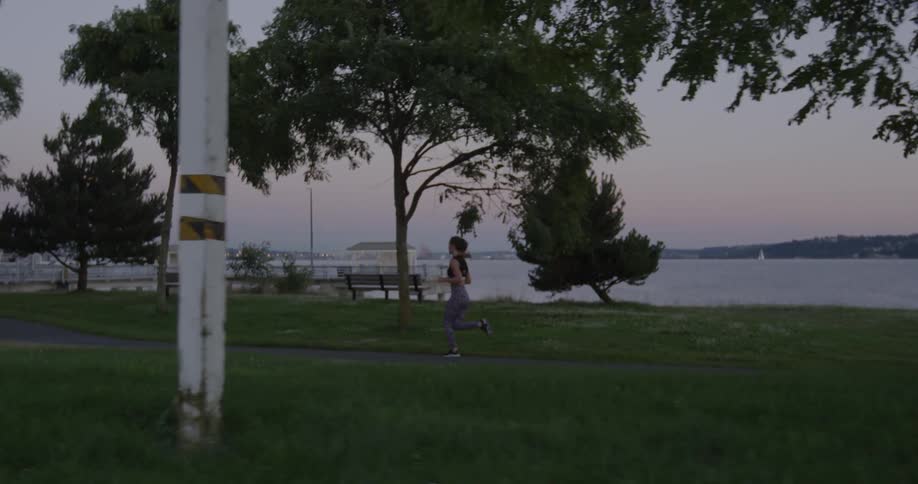 A female jogger is running in a park near a harbor