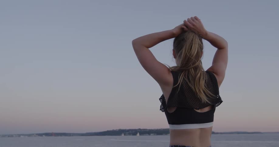 Woman looking at a large body of water while standing and resting her hands on top of her head