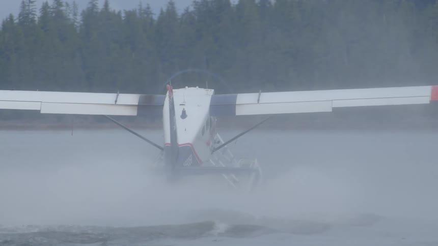 A powerful seaplane creates a wake of mist on a lake with a forest in the background