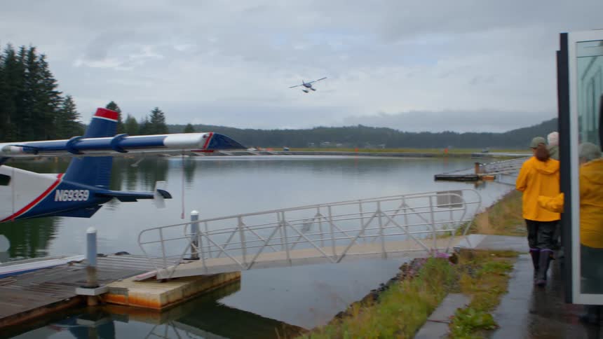 A seaplane takes off from a remote Alaskan lake as passengers disembark from a tour bus to watch