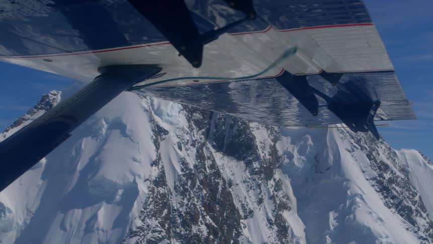 An aerial point-of-view from under a plane's wing captures the majestic beauty of a vast, snowy mountain landscape