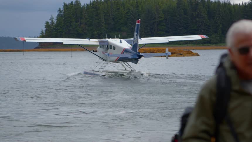 A guide and tourists walk along a remote shore as their seaplane taxies away in the background