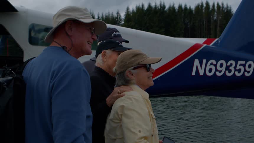 A group of happy tourists take photos with a smartphone next to a seaplane docked on a scenic lake