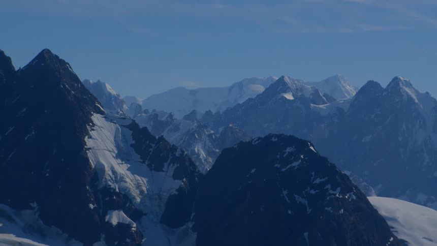 A breathtaking static shot of a vast, snow-covered mountain range under a clear blue sky