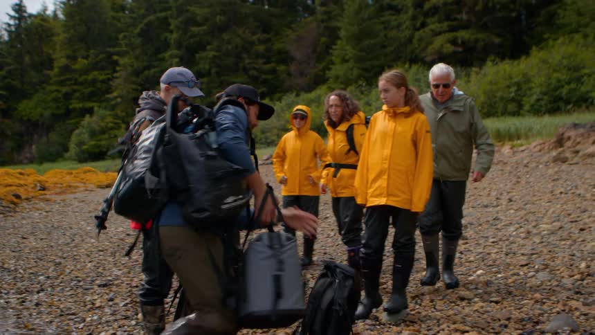 A guide unloads expedition gear from a seaplane for a group of tourists on a remote, rocky shoreline