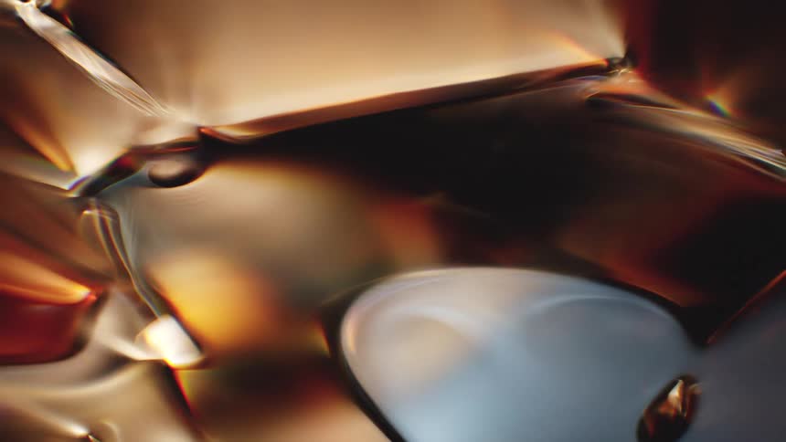 A mesmerizing macro view of a fluid, glassy surface with slowly shifting highlights and shadows in warm amber and cool metallic tones