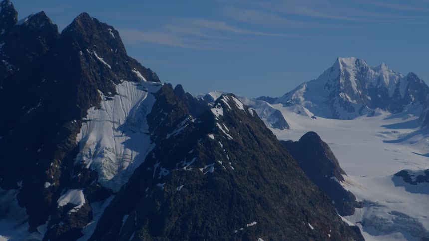 A serene timelapse captures the immense beauty of a rugged, snow-capped mountain range and its sprawling glaciers