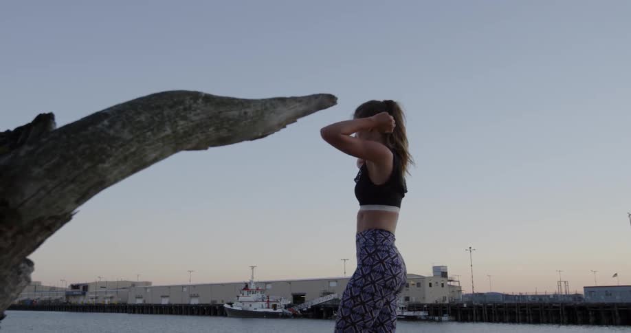 A woman walks next to a body of water in a sports bra at sunset