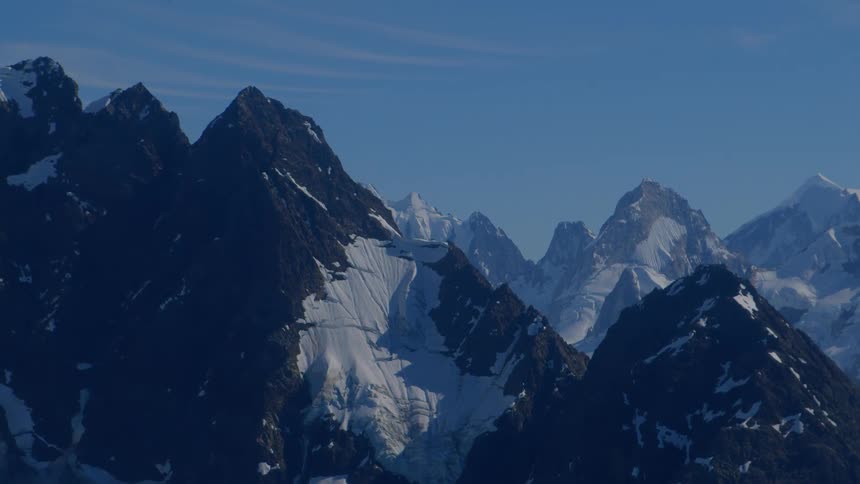 Slowly zooming in on the majestic snow-capped peaks of a remote mountain range against a clear blue sky