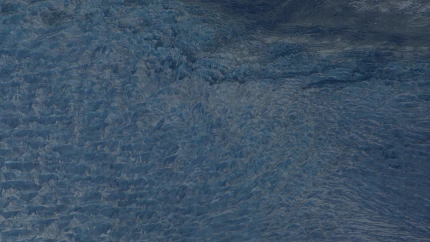 A slow aerial pullback reveals the vast and heavily textured blue ice field of a massive glacier