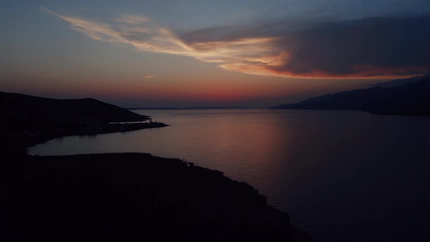 An ethereal aerial view of a tranquil coastal bay at dusk, where the last fiery glow of sunset illuminates the sky and reflects on the calm water