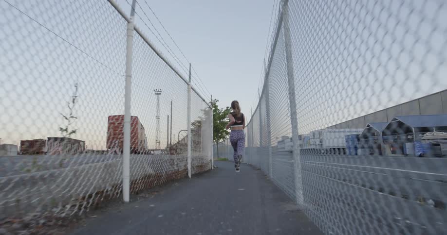 A female jogger is running on a fenced in path near train cars