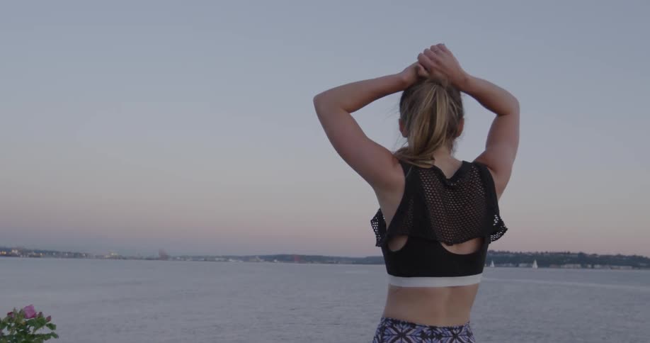 A female jogger is stopped at the edge of a harbor looking around