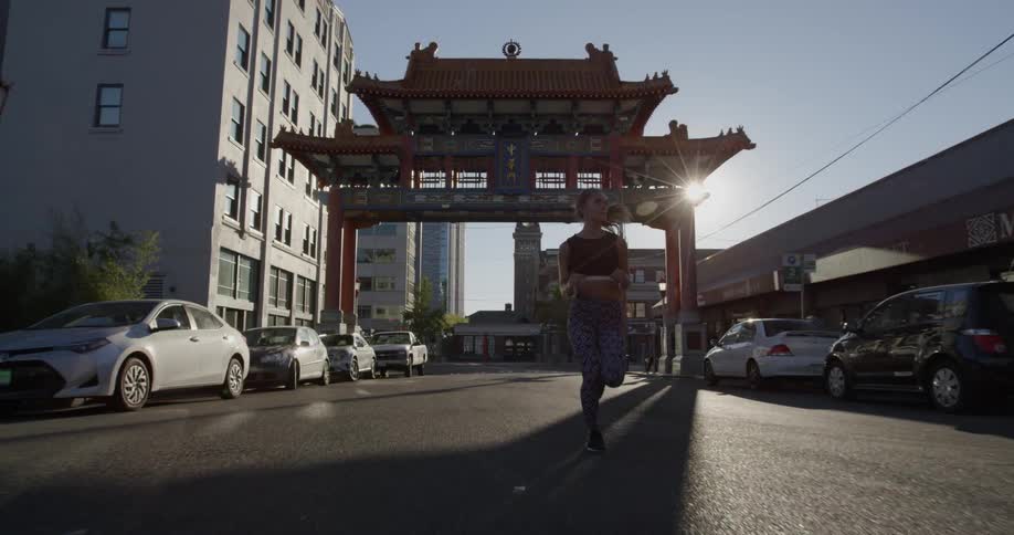 A woman is jogging in a street near a chinese gate