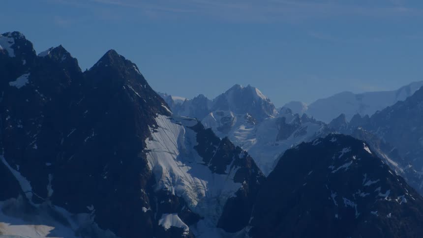 A stunning slow zoom out of a majestic snow-capped mountain range under a clear blue sky