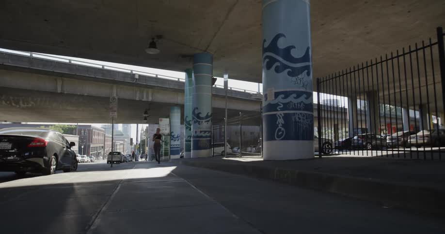 A woman is jogging beneath a freeway during the day