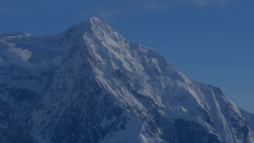 A slow pan reveals the majestic, snow-covered peaks of a vast mountain range against a clear blue sky