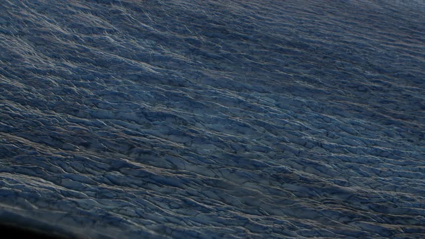 Slow aerial tracking shot over the vast, textured, and crevassed surface of a blue ice glacier