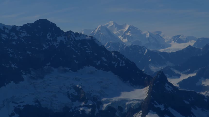 Expansive view of a snow-covered mountain range, with sunlit white peaks towering in the background under a clear blue sky