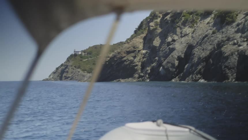 A point of view from a small dinghy sailing towards the rugged, rocky cliffs of the Mediterranean coast on a sunny day