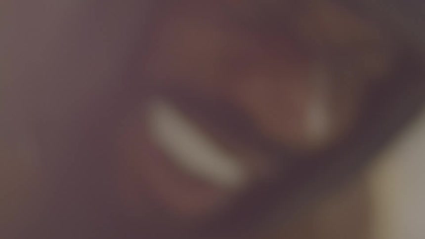 A blurry, low-angle, extreme close-up of a smiling man in a dark hoodie