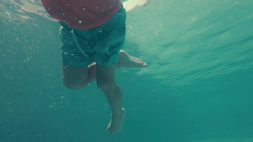 An underwater slow-motion view of a young child in a life vest floating serenely in a sunlit swimming pool