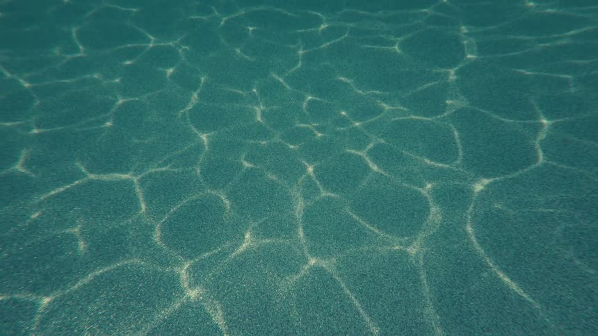 A serene underwater shot of sun rays forming caustic patterns on the sandy ocean floor