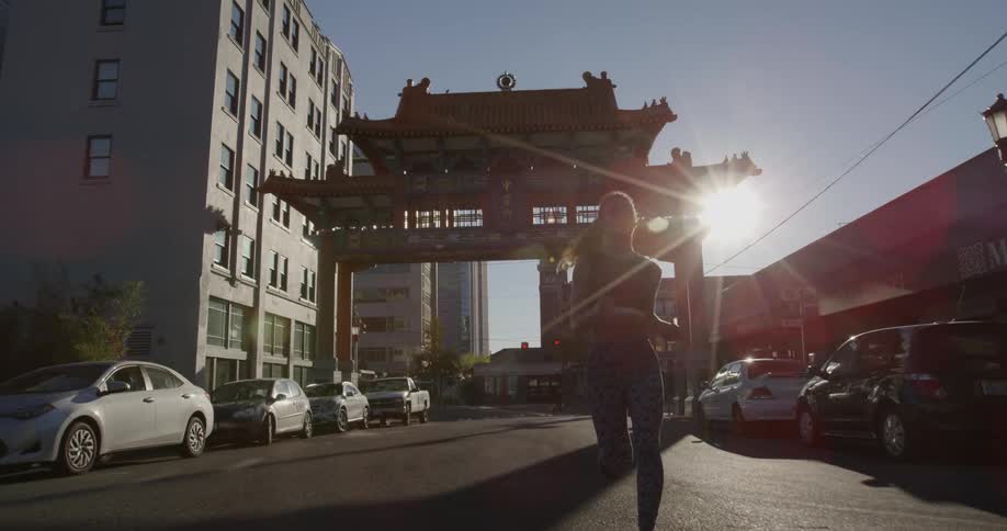 Woman jogs down a car lined street in the city