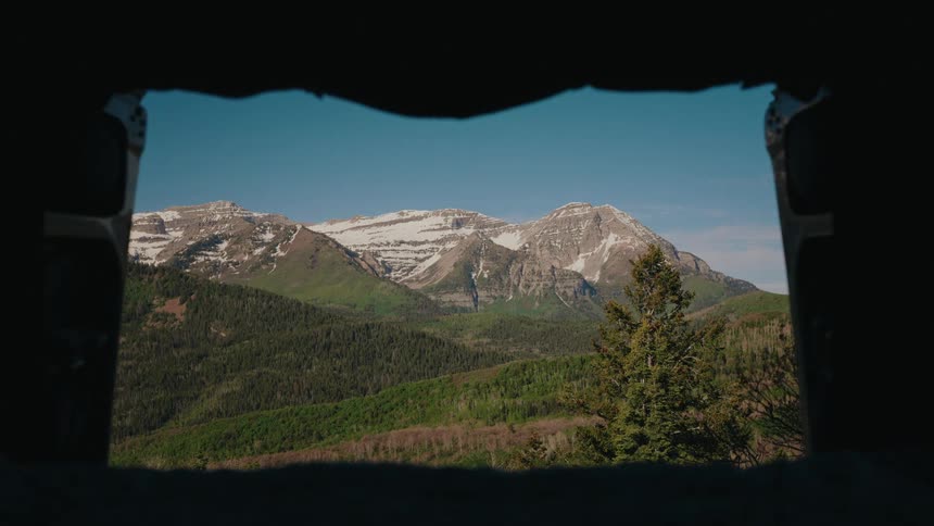 A breathtaking view of snow-capped mountains and lush green forests from the window of a camper van