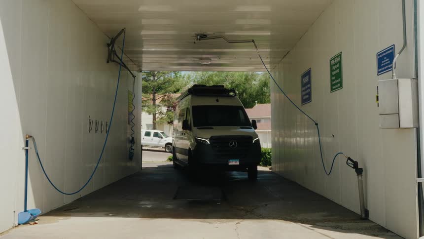 A modern camper van slowly pulls into a self-service car wash stall to be cleaned