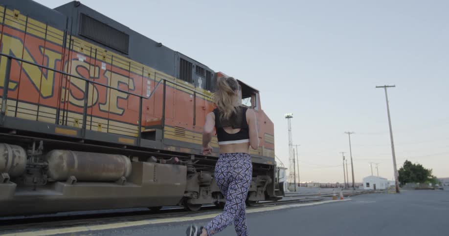 Woman jogging next to a locomotive engine on its tracks
