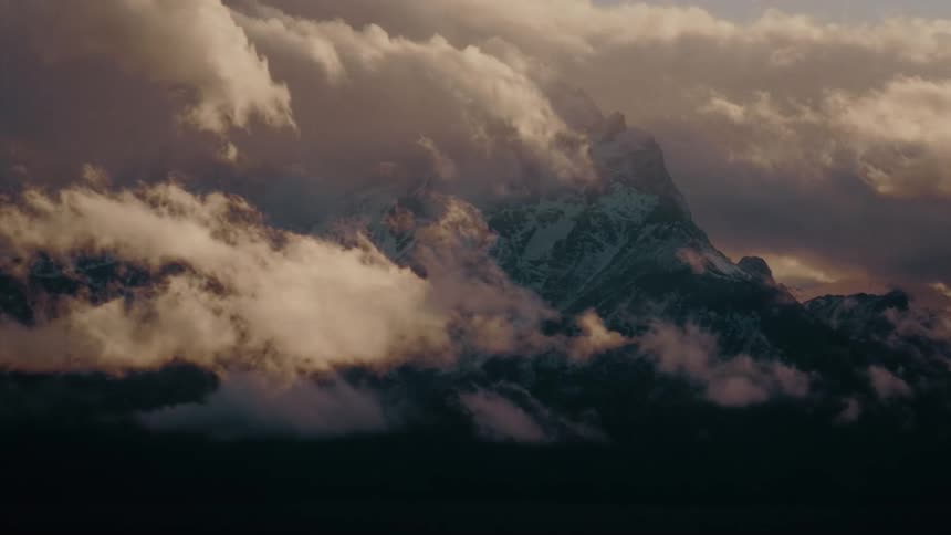 A majestic snow-capped mountain peak is shrouded in dramatic, golden-lit clouds