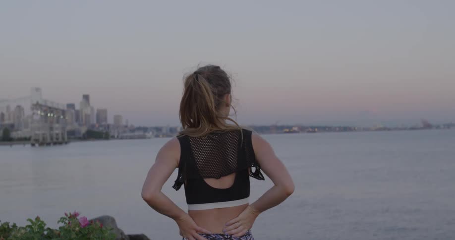 A woman wearing workout clothes stands near a body of water