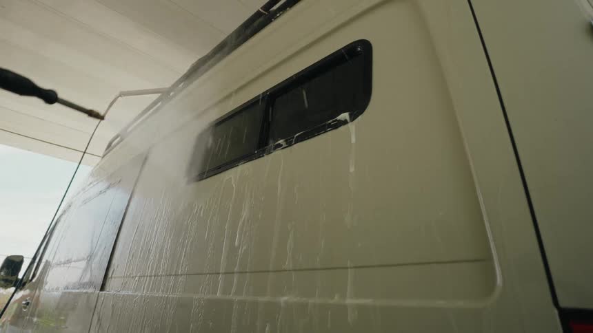 A low-angle, slow-motion shot of a white camper van being cleaned with a high-pressure washer