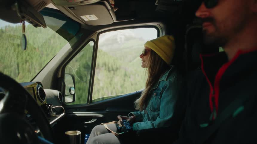 A young woman in a yellow beanie enjoys the mountain scenery from the passenger seat of a moving van