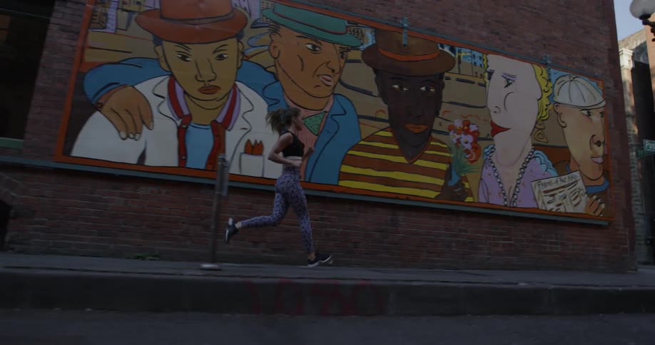 A woman is jogging past a mural on an urban building