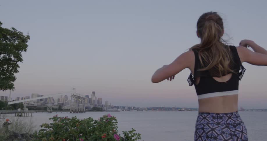 A female jogger catches her breath as she stops near a harbor at dusk