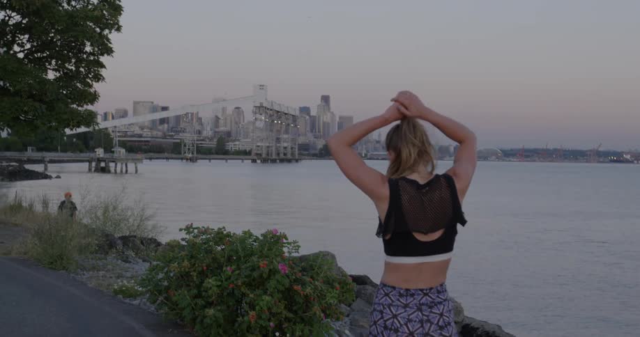A woman walks along the water then raises her hands