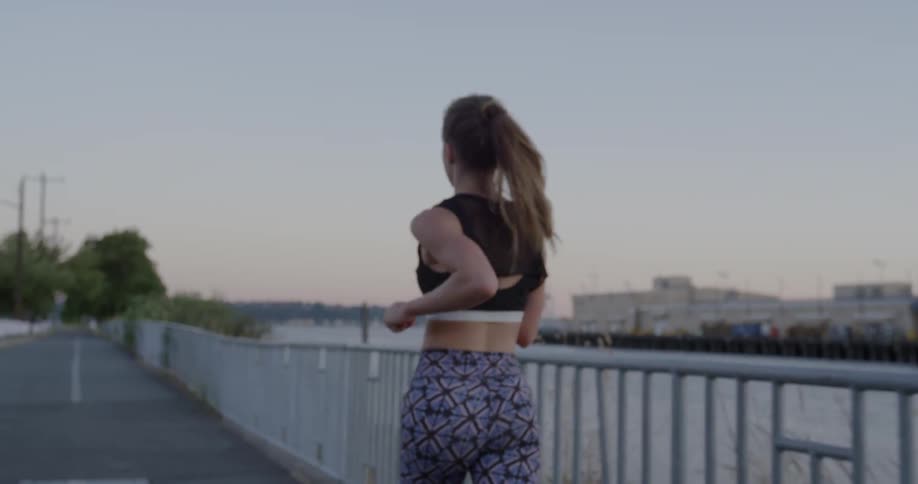 A woman jogs near a river while wearing a sports bra
