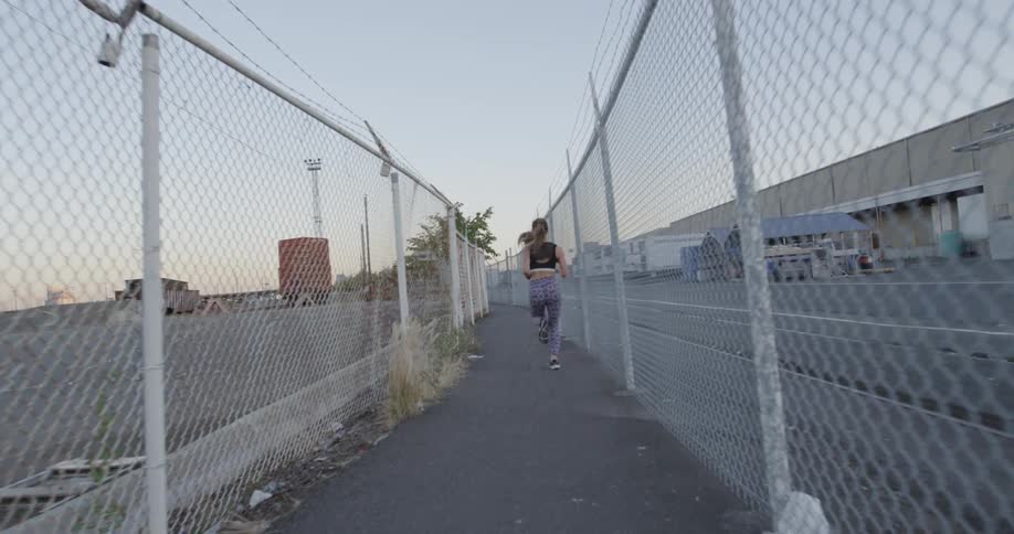 A woman is running down a trail surrounded by fences