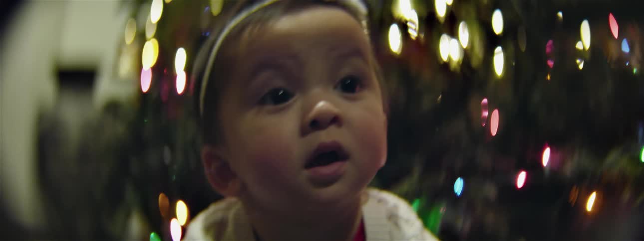 A baby looks around by a christmas tree