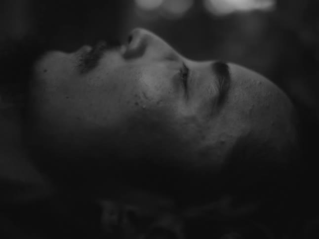 A moody black and white close-up of a person's face with their eyes closed in the dark