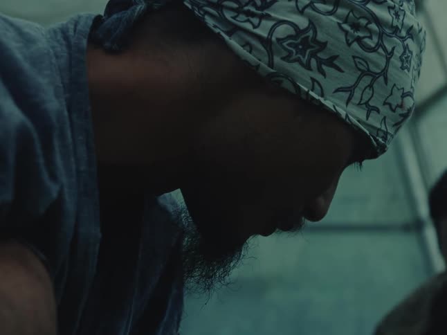 A close-up profile of a man with a beard and bandana concentrating in a dimly lit environment