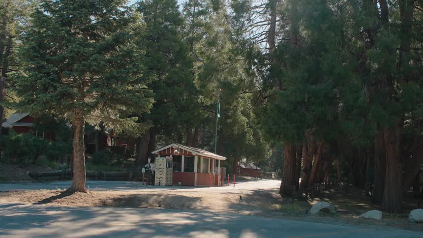 A park ranger stands guard at the entrance booth of a sunny, forested national park campground