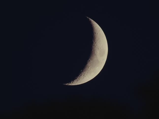A detailed close-up shot of a waxing crescent moon with visible craters against the blackness of space