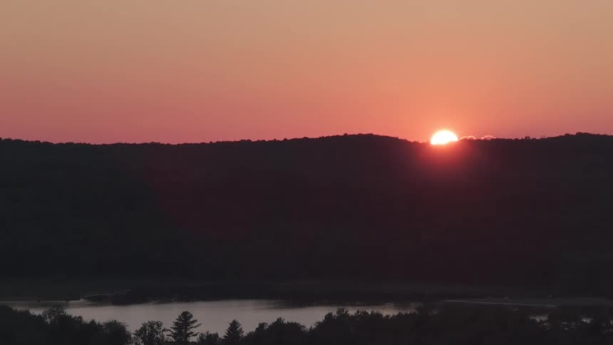 A beautiful time-lapse of a sunrise cresting over a silhouetted hill, revealing a misty lake in the valley below