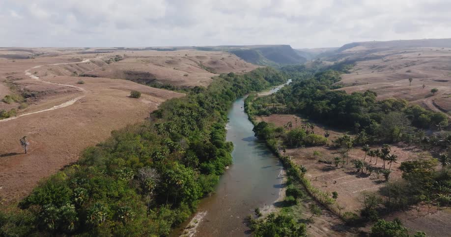 Aerial footage captures a serene river winding through a vast valley of arid, rolling hills and lush, green trees