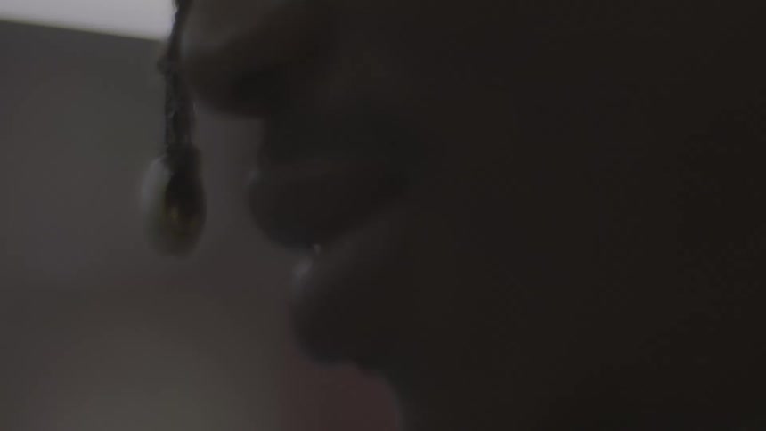 An extreme close-up of a person's mouth in silhouette as they chew and talk in a dark room